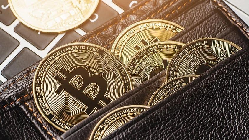 Bitcoin coin in a leather wallet on a computer keyboard.