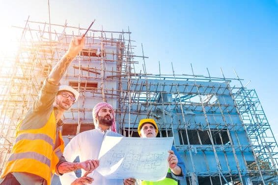 Dubai house construction, scaffolded building in front, Emirati citizen holding a blueprint, consulting with two construction engineers.