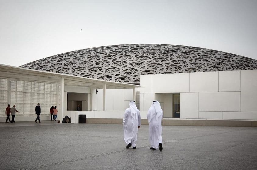 Tourists at the Louvre Abu Dhabi museum and two people in white traditional Emirati clothing.