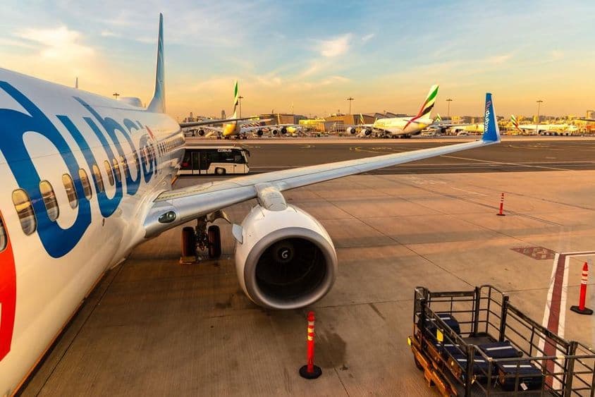Flydubai plane parked with multiple other planes in the background and a passenger transport bus, right with luggage on a small transport vehicle.