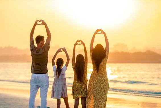People on the beach with their backs to the camera, forming a heart with their hands, with the sea in the background.