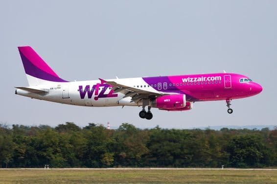 Wizz Air plane flying at low altitude with a forest in the background.
