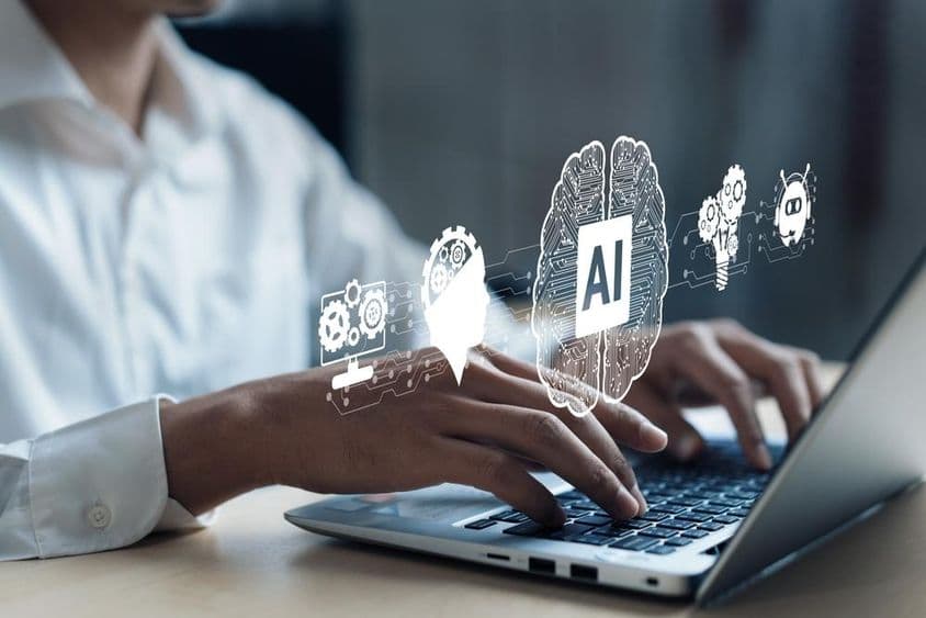 Projection over a notebook showing an AI brain and other elements. A human hand working on the computer.