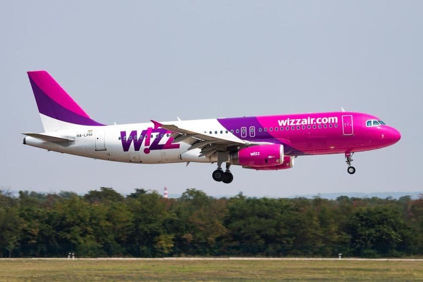 Wizz Air plane flying at low altitude with forest in the background.