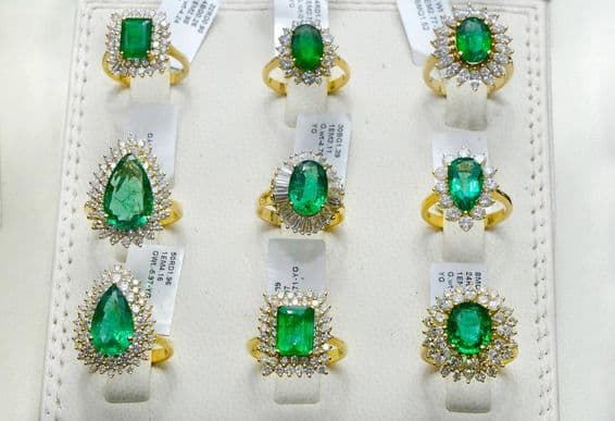 Emerald rings surrounded by diamonds on a gold band.