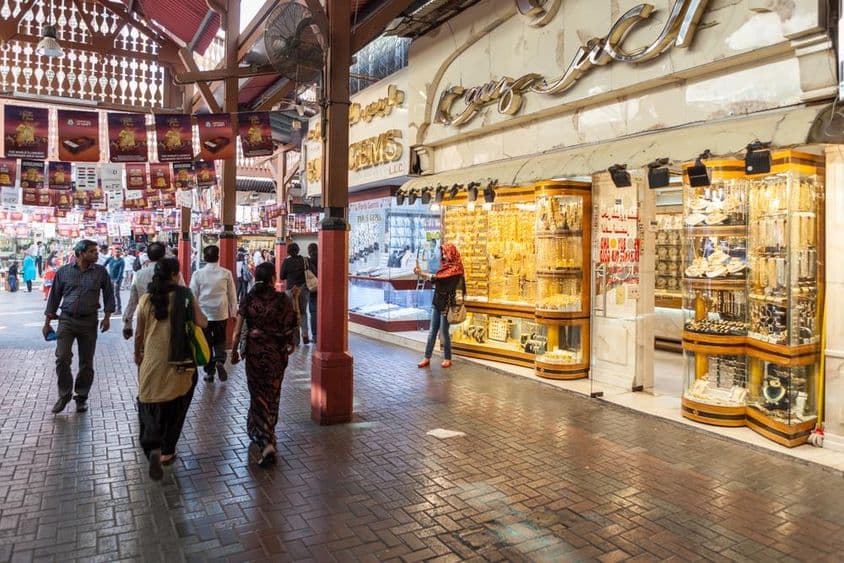 Dubai gold market, a store showcasing gold jewelry, with people walking by.