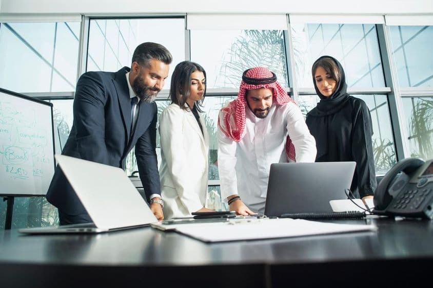 Company executives deliberating in an office with laptop and phone in front.