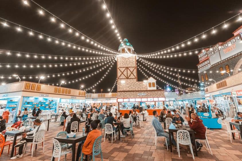 Global Village, tourists and locals tasting food specialties at tables.