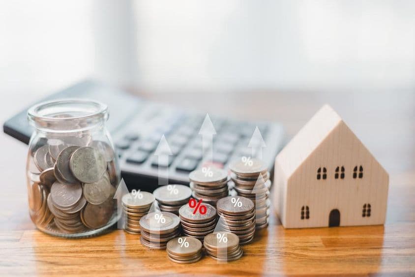 Coins in a mason jar, coins piled next to it, with a keyboard in the background, and a wooden building beside it.