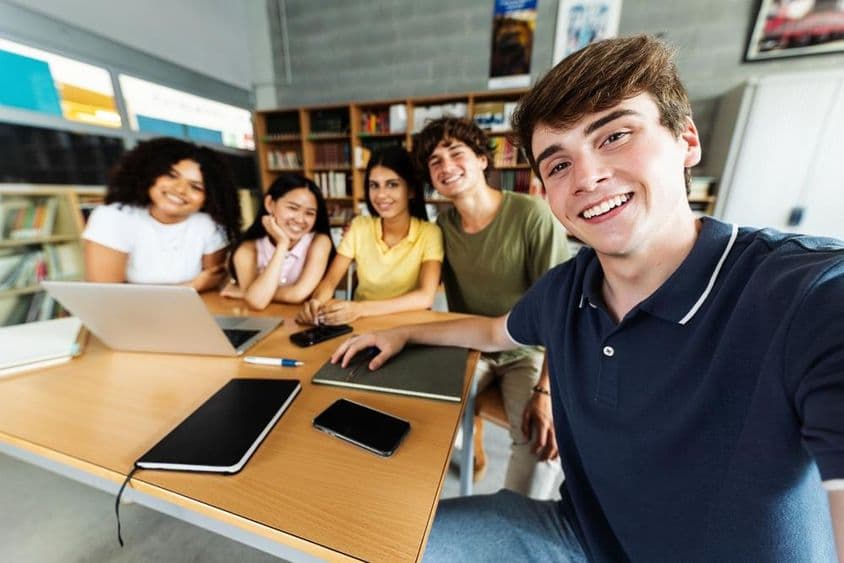 Students studying in the library, with a notebook, phone, and paper notepad on the desk.