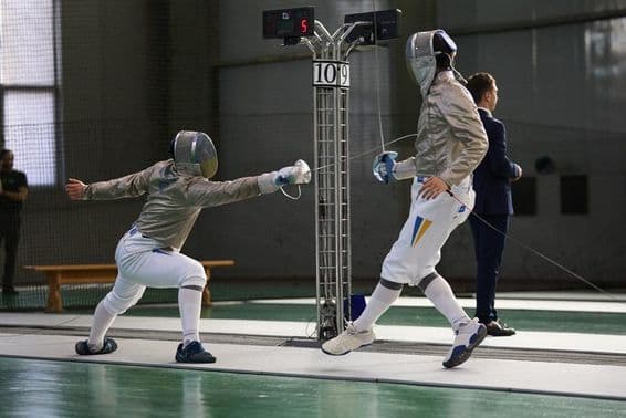 Two fencers competing on the piste, one scoring a hit.