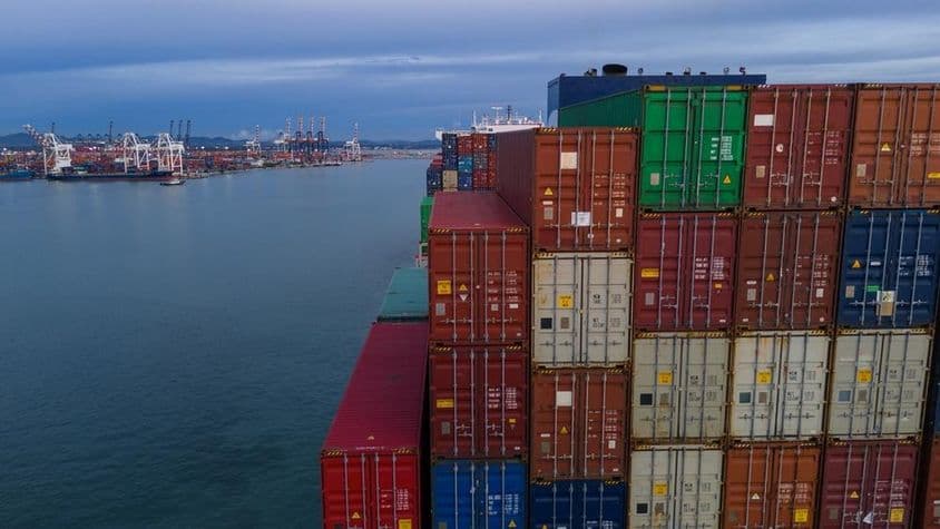 On the left, a bay of a sea port is visible, to the right stacked containers.