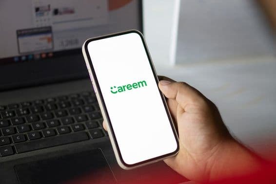A hand holds a phone running the Careem app, with a notebook visible in the background.