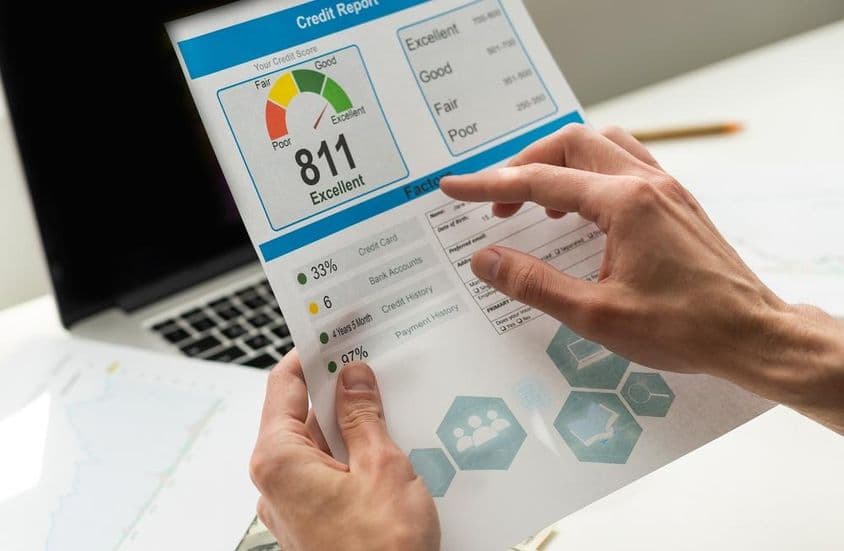 A person reading a bank credit score with a hand visible, background showing a turned-off laptop.