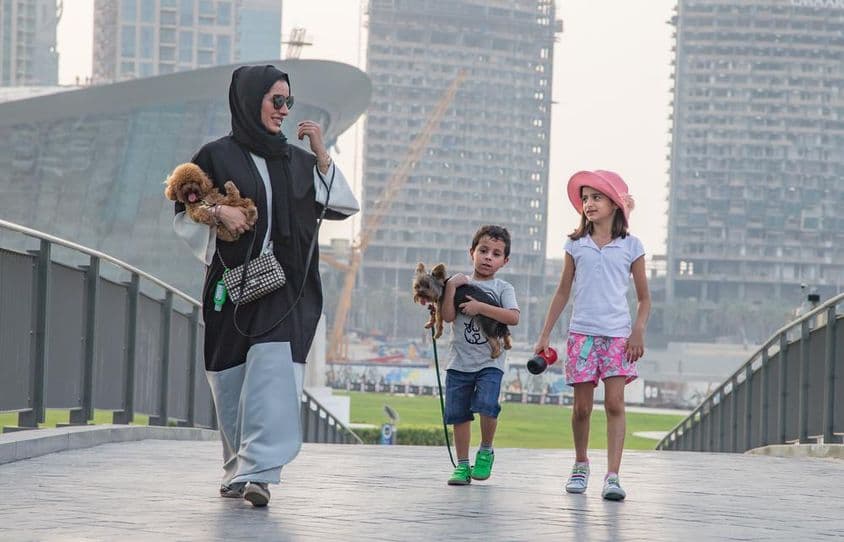 A family of four in front of Dubai skyscrapers, with the mother and one child holding a dog.