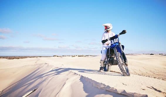 Person motorcycling in the desert, wearing white clothes on a blue motorcycle.