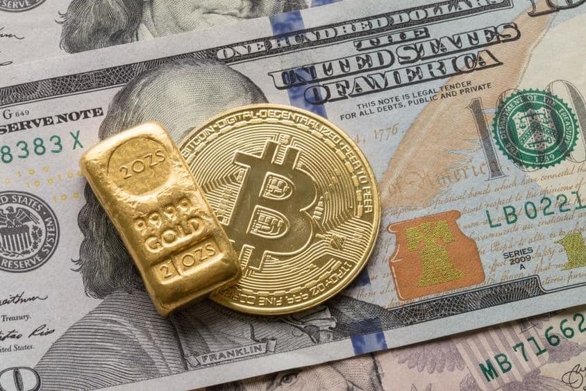 An investment gold bar and a Bitcoin coin over a 100 dollar bill.