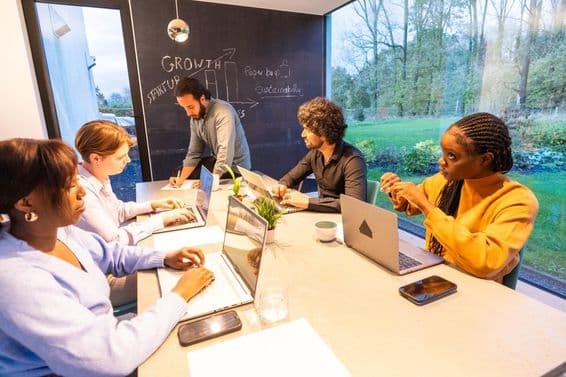People sitting at a table with laptops, discussing something.