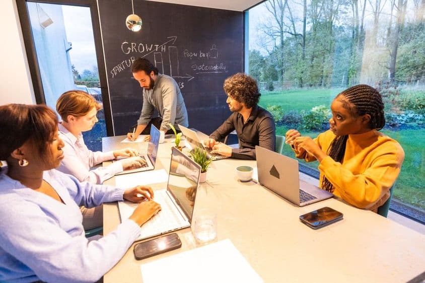 People sitting at a table with laptops, discussing something.