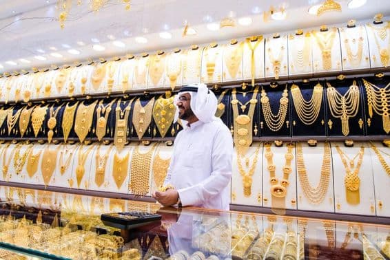 Dubai gold vendor, with a background of many gold necklaces, the vendor in traditional white attire.