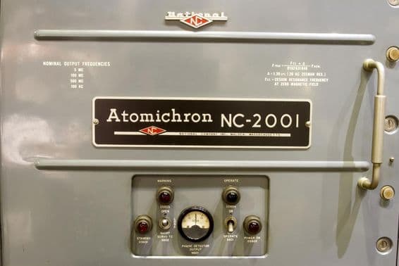 Displayed is the control panel of an old atomic clock, along with its name on a small plate.