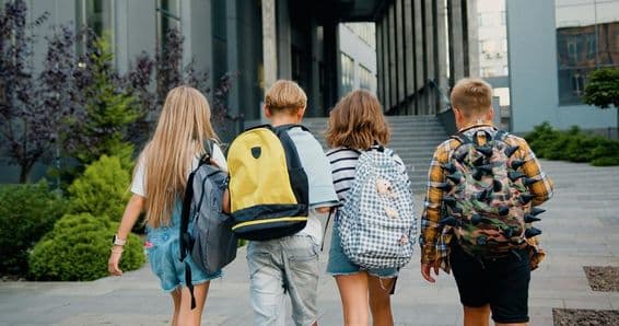 Students carrying backpacks in front of a school entrance.