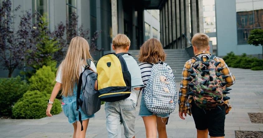 Students carrying backpacks in front of a school entrance.