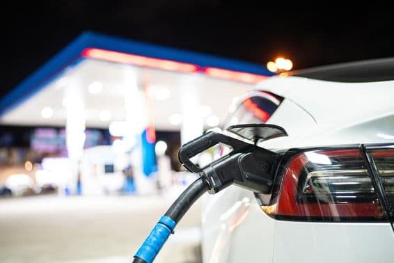 A Tesla being charged, with a gas station in the background.