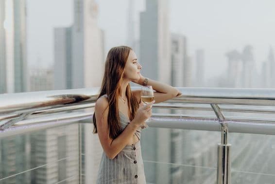 Young girl on a terrace with a glass of wine, blurry Dubai skyscrapers in the background.