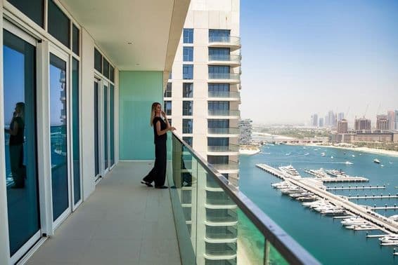 A woman on a Dubai terrace observing boats on the canal with a skyscraper in the background.