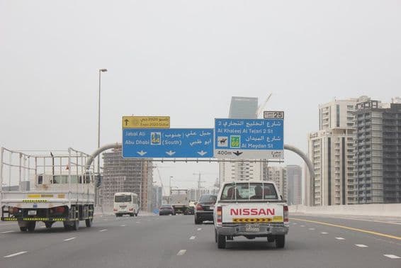 Al Khail Road overhead road sign, with a few tall buildings in the background.