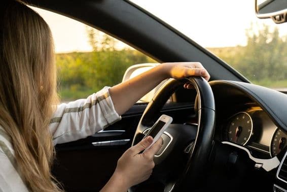 A woman using a mobile phone while driving, holding the steering wheel with the other hand.