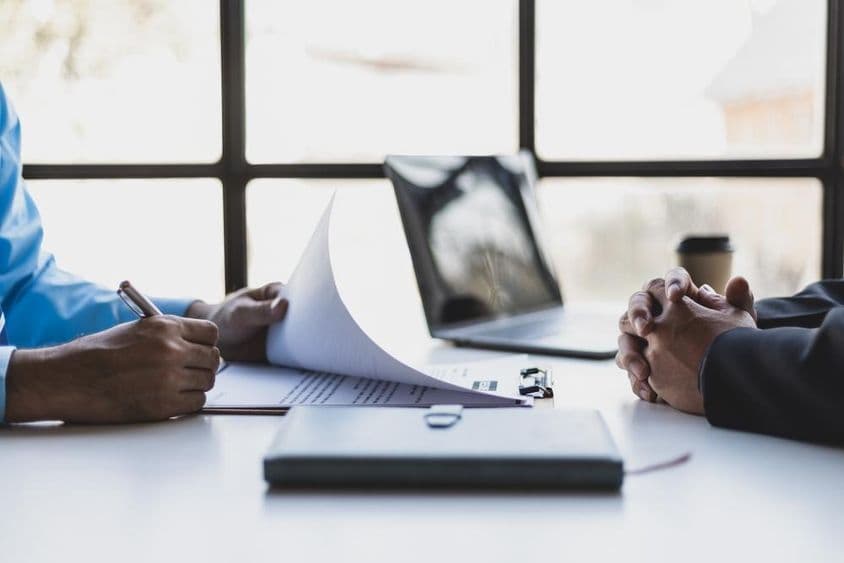 Two individuals seated across from each other during a job interview, with a notebook placed on the table between them.