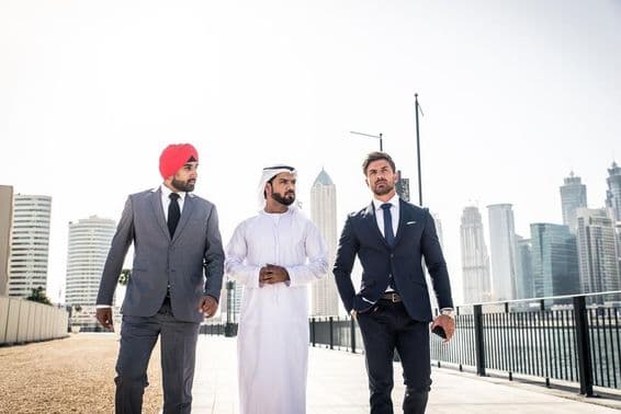 An Indian, an Emirati, and a European citizen walking along the canal, skyscrapers behind them.