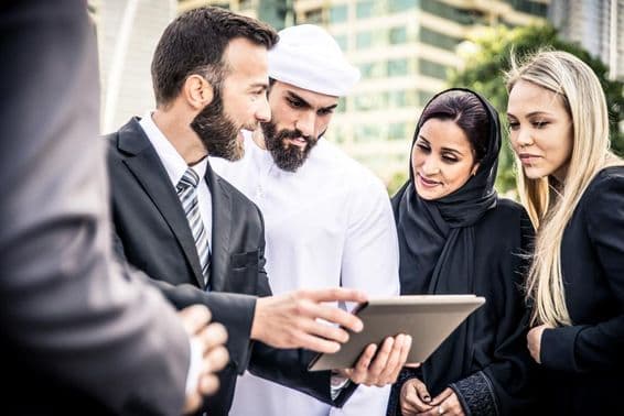 A European and an Emirati man looking at a tablet flanked by two women, a blonde and an Emirati, observing.