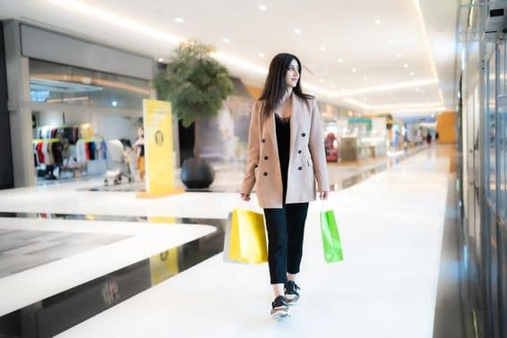 A woman shopping in Dubai Mall, holding two bags, with shops in the background.