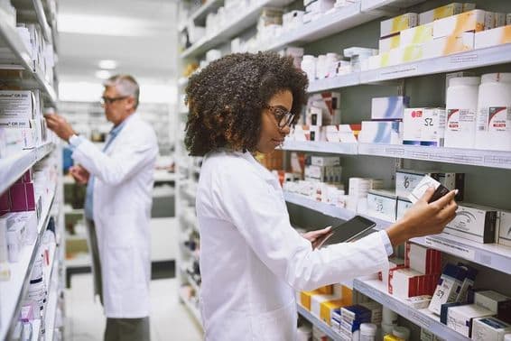 A pharmacy shelf being stocked by a woman and a man checking medications.