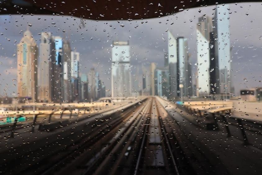 Rain seen through a Dubai metro window with skyscrapers in the background.