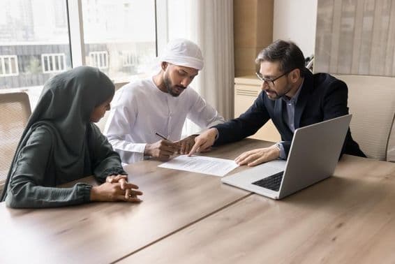 An Emirati family signing a contract in front of a broker, with a notebook on the table.