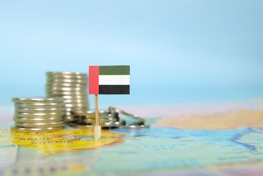 A UAE flag embedded in a map, with stacked coins beside it.