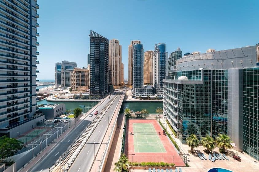 A tennis court in Dubai with skyscrapers and a speedboat on the water.