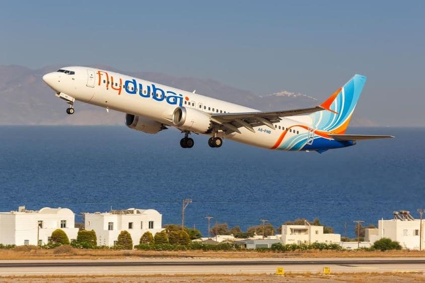 flydubai aircraft flying at low altitude, with small white houses and the sea in the background.