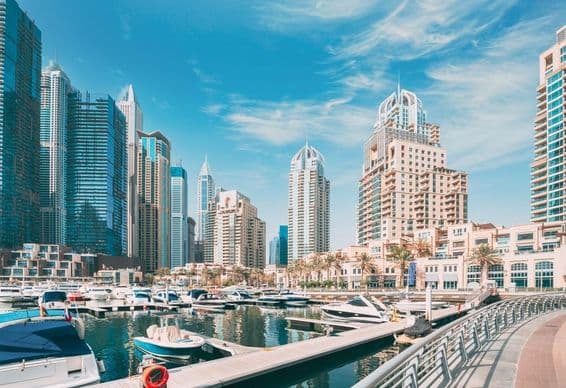 Dubai skyline with marina harbor, boats floating, skyscrapers in the background.