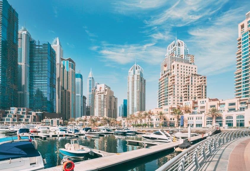Dubai skyline with marina harbor, boats floating, skyscrapers in the background.