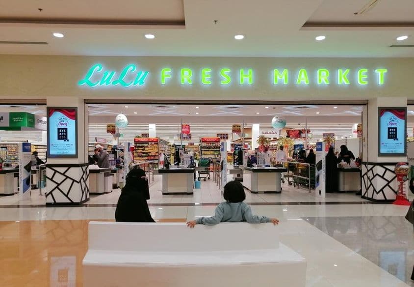 Entrance to a LuLu store in a mall, with two people sitting, a woman and a child, seen from behind.