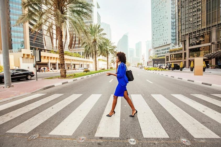 In Dubai, a woman crosses a zebra crossing on an empty road, with houses visible in the background.