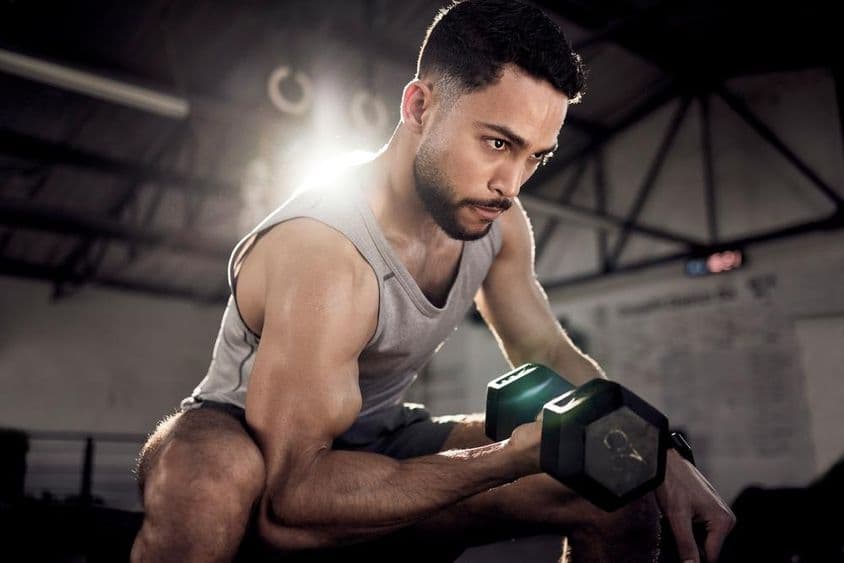 A muscular man strengthening his biceps with a small dumbbell in a gym.