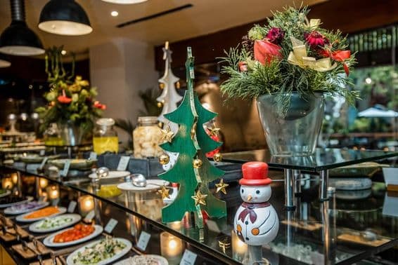 Small snowman in a restaurant on a vegetable counter, next to a wooden Christmas tree.