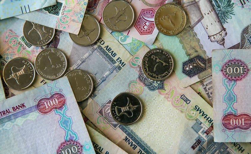 Dubai paper currency scattered on a table with 1 dirham coins above.