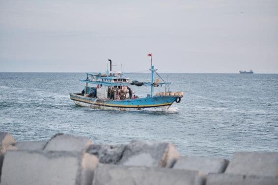 A weathered fishing boat on the sea with people onboard.